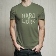 Male model wearing a green t-shirt with 'HARD AT WORK' text against a wooden panel background
