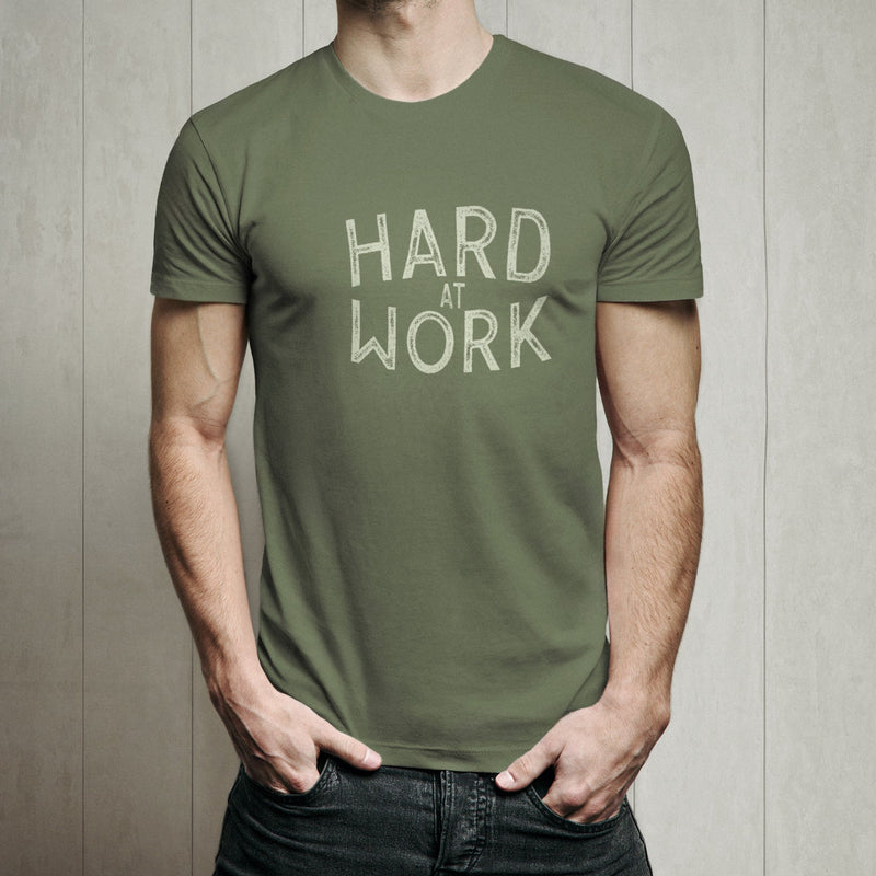 Male model wearing a green t-shirt with 'HARD AT WORK' text against a wooden panel background