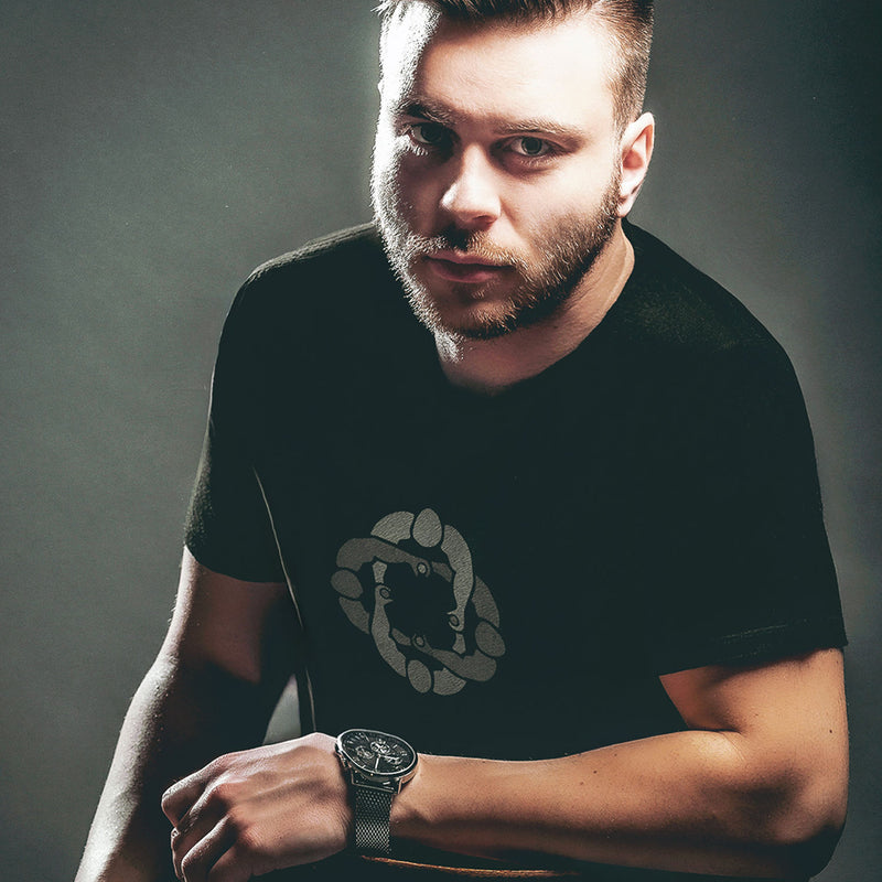 Model wears black cotton t-shirt with subtle circle graphic of seated male figures holding hands (Circle Jerks), viewed from above; gay-themed design for bators and group play