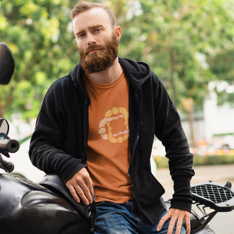 Model wears orange cotton t-shirt with subtle circle graphic of seated male figures holding hands (Circle Jerks), viewed from above; gay-themed design for bators and group play