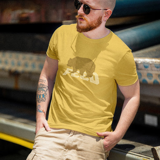 A man wearing a mustard yellow graphic t-shirt with a bear design, khaki cargo shorts, and sunglasses, posing outdoors in front of a shipping container.