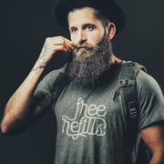 Man with a beard wearing a gray, Graphite Heather t-shirt with 'Free Refills' typographic design printed on front and a backpack; on a dark background