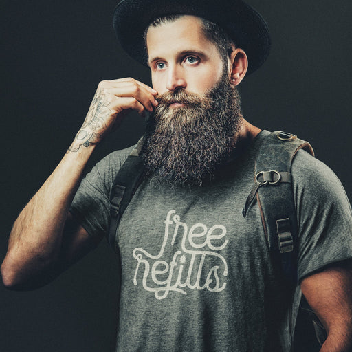 Man with a beard wearing a gray, Graphite Heather t-shirt with 'Free Refills' typographic design printed on front and a backpack; on a dark background