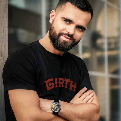 Sexy, bearded male model wears the black "Girth" T-shirt | A slightly arched  typographic design made with red patterned letter forms printed on tee, towards top of breast plate