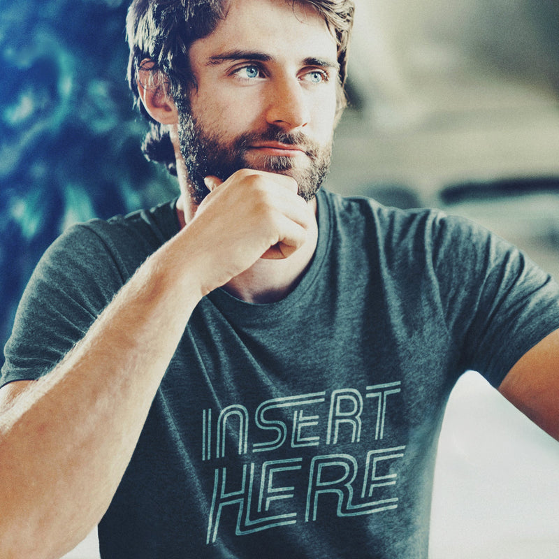 PRODUCT IMAGE: 'Insert Here' T-shirt | Suggestively raunchy tee for horny gay bottom guys | Handsome male model, with hand on chin, looking up towards top right corner wears Dark Heather tee with a white distressed typographic design is printed on it, in the chest area 