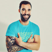 PRODUCT IMAGE: 'Insert Here' T-shirt | Suggestively raunchy tee for horny gay bottom guys | Handsome male model, arms crossed, slightly hunched over, big smile, wears Turquoise tee with a yellow distressed typographic design is printed on it, in the chest area 