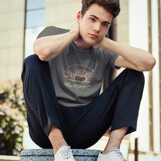 Model wears Charcoal shirt with a woodcut-style linedrawing of a pink pig with typography below, revealing the design's name, "This ‘Lil Piggy T-shirt"; Funny Gay SFW Tee for Horny Gay Guys Who are Quietly Nasty Pigs