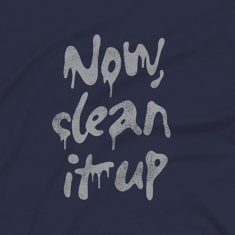 Close up of a navy t-shirt with "Now, clean it up" printed on the chest; the  milky white letterforms drip, lending to an appropriate interpretation