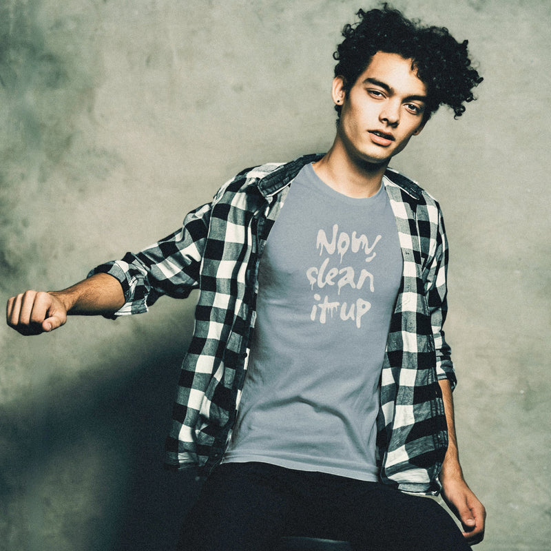 Young, thin male model sits on a sits on a stool, wearing a steel blue t-shirt with "Now, clean it up" printed on the chest; the  milky white letterforms drip, lending to an appropriate interpretation