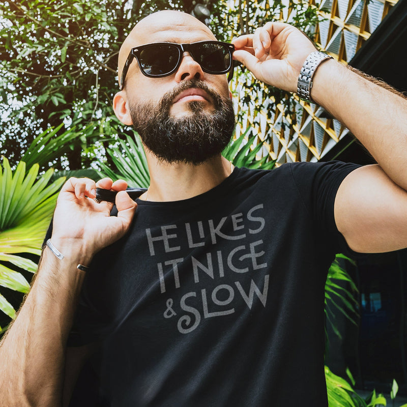PRODUCT IMAGE: He Likes It Nice & Slow T-shirt | Funny Gay Tee for the guys who take their time and enjoy the ride | Model wears Black shirt with a design borne out of retro-inspired typography