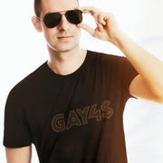 Model wears brown GAY4$ shirt with bold, bling-inspired typography — a cheeky, provocative tee for queer men and hustlers alike.