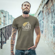 A sexy bearded model poses on an urban walkway wearing an Army t-shirt with a graphic featuring a rugged, bearded biker in a distressed vintage print style with the design's namesake, "Ride It."