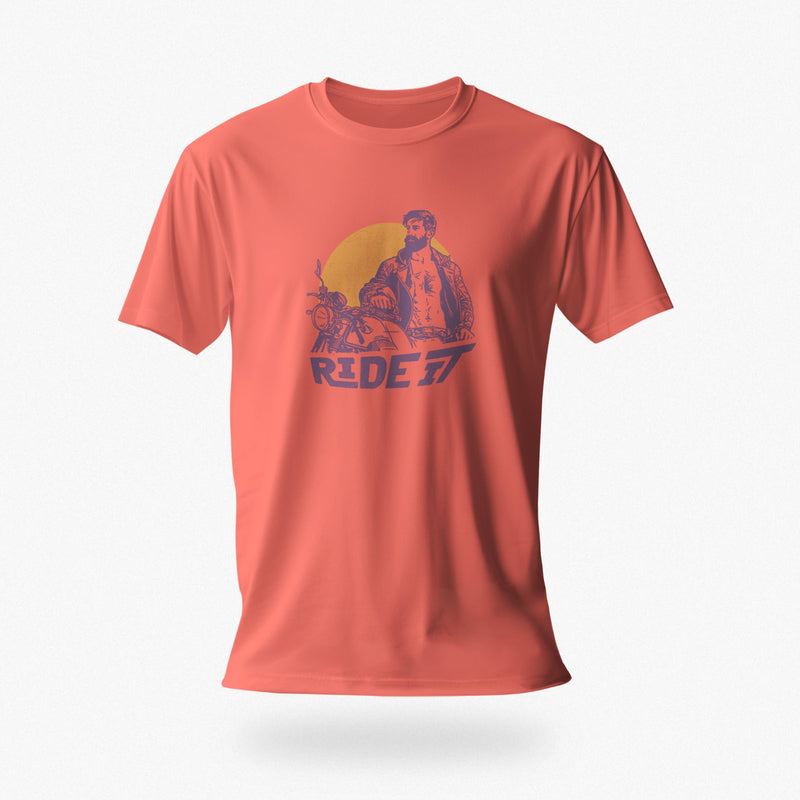 PRODUCT IMAGE of a coral silk t-shirt with a graphic featuring a rugged, bearded biker in a distressed vintage print style with the design's namesake, "Ride It."