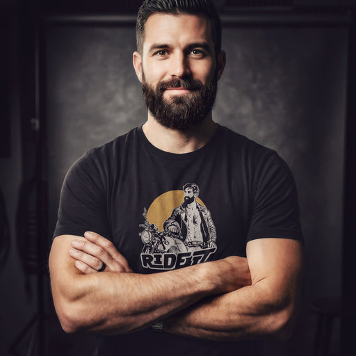 A sexy bearded model poses in a studio wearing a dark gray t-shirt with a graphic featuring a rugged, bearded biker in a distressed vintage print style with the design's namesake, "Ride It."
