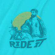 A close-up detail of the graphic printed on a turquoise tee featuring a rugged, bearded biker in a distressed vintage print style with the design's namesake, "Ride It."