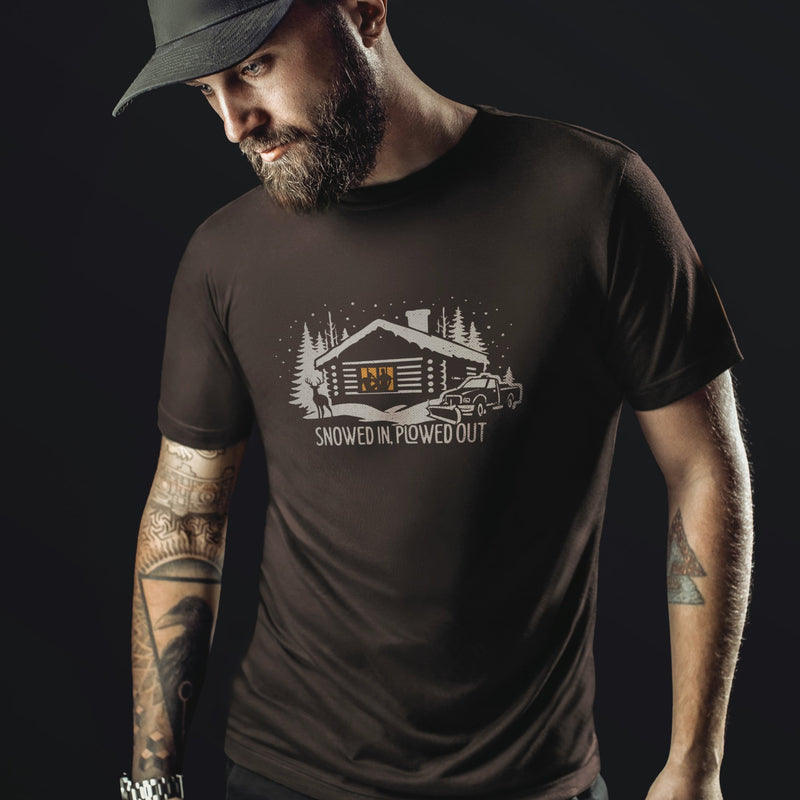 Men’s graphic t-shirt showing a snowy log cabin and plow truck, featuring the phrase “Snowed In, Plowed Out,” a subtle innuendo design for gay men. Bearded male model wears brown tee.