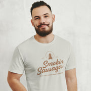 Male model wearing a 'Smokin Sausages' t-shirt with a logo on a plain background
