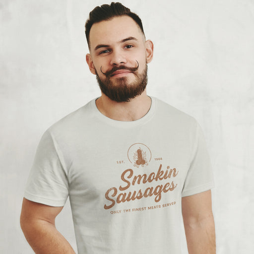 Male model wearing a 'Smokin Sausages' t-shirt with a logo on a plain background