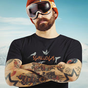 Tattooed model w/ snowboarding goggles wears black "Swallows" t-shirt; graphic white swallows fly around and perch on the coral-colored word "swallows" | Gay Humor, Queer AF Tee for Guys who Live for Every Drop