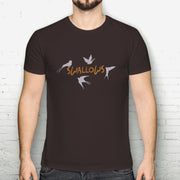 Person wearing a dark brown t-shirt with 'SWALLOWS' design against a white brick wall.