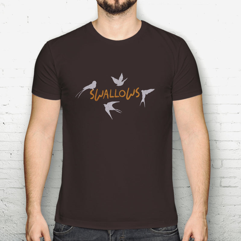 Person wearing a dark brown t-shirt with 'SWALLOWS' design against a white brick wall.