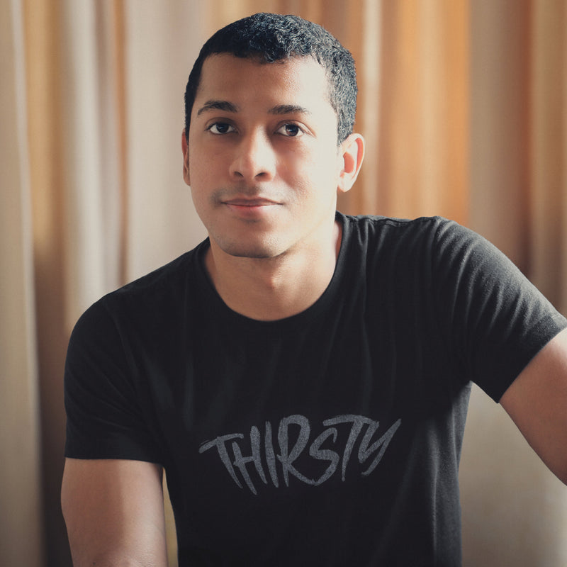 Model wears black Thirsty T-shirt | Raunchy Tees for Horny Gay Guys Who Thirst for It | Model wears Light Gray heather shirt with a typographic design