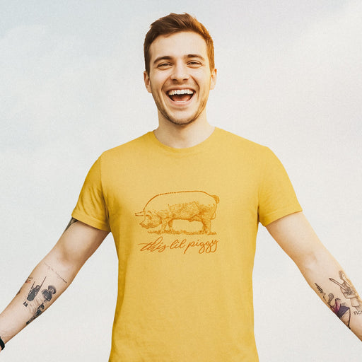 Model wears Mustard t-shirt with a woodcut-style line drawing of a pink pig with typography below, revealing the design's name, "This ‘Lil Piggy T-shirt"; Funny Gay SFW Tee for Horny Gay Guys Who are Quietly Nasty Pigs