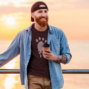 Trail | Raunchy T-shirt for Horny Gay Bears on the Hunt | Man wearing a oxblood t-shirt with a white paw print design leans against a railing, with sun setting in the horizon